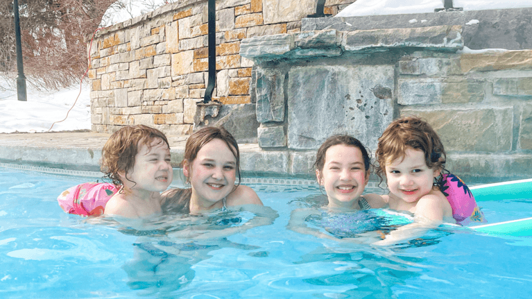 Four kids relax in an outdoor pool.