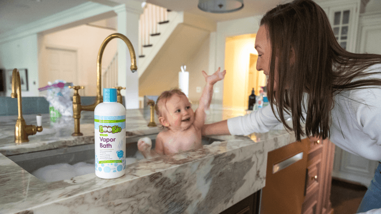 A mom gives her baby a bubble bath in her kitchen sink.