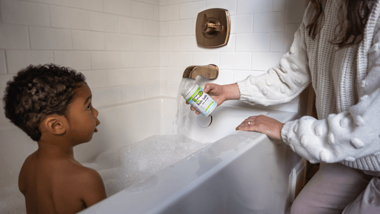 A mom pours bath salts into her child's bubble bath.