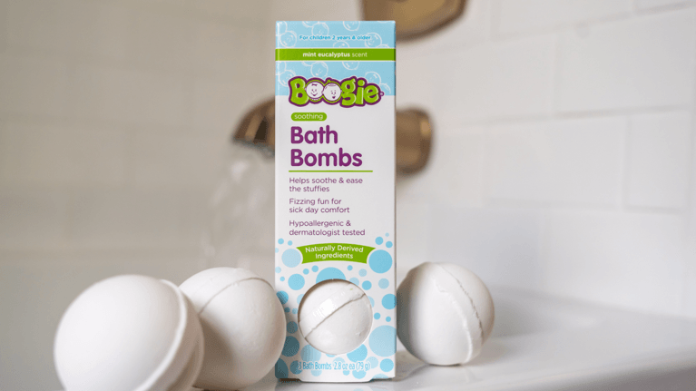 A package of the Boogie Soothing Bath Bombs are displayed on the edge of a bathtub.