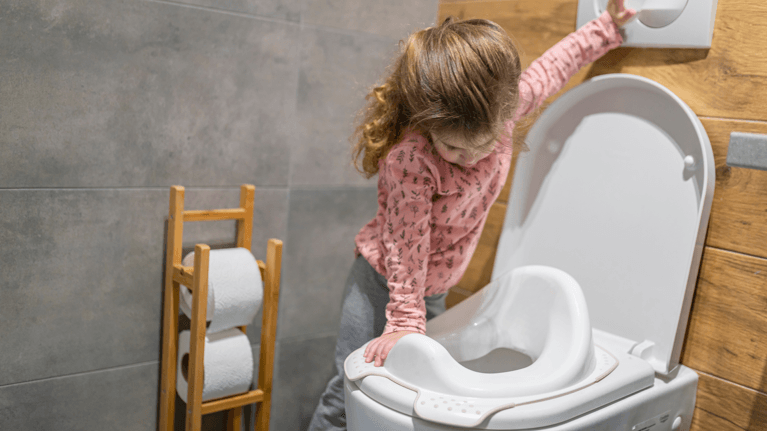 A little girl flushes a toilet in the bathroom.