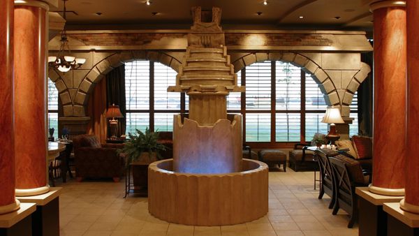 Photo of a Dimly lit room with a fountain in the centre. There are rounded windows in the back ground and seating around the fountain