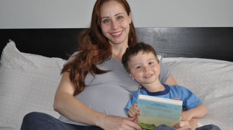 Smiling pregnant mom and young son on bed