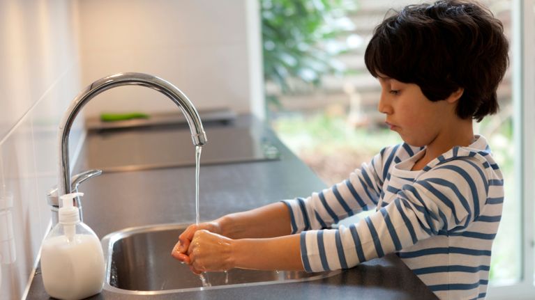 An eight-year-old boy washes his hands at a kitchen sink.