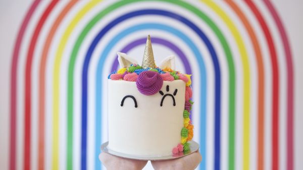 someone holding up a unicorn cake in front of a rainbow