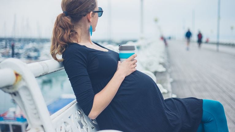 pregnant woman sitting on a bench with coffee