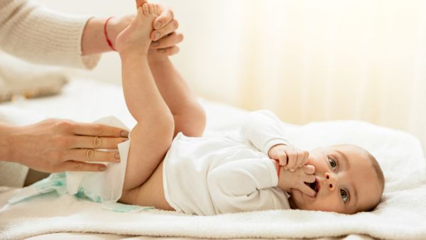 Baby boy lying on the bed with hands in the mouth while getting his diaper changed.