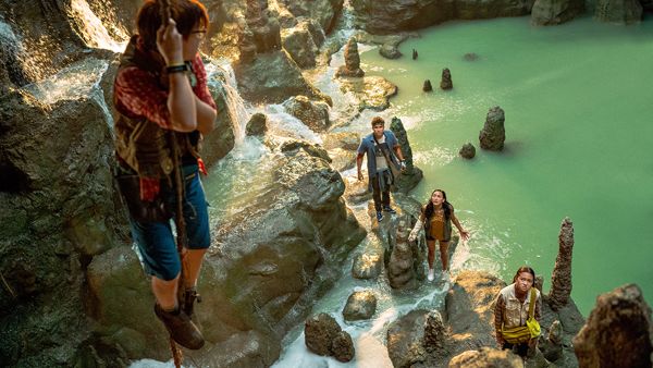 A still from Finding Ohana showing a kid hanging from a rope in a cave while their friends shout up at them from the ground