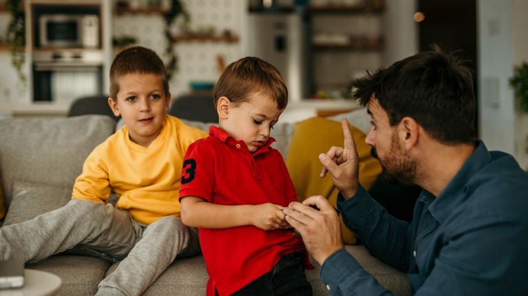 An annoyed man is teaching his son and his brother how to behave while sitting on the sofa at home during the day.