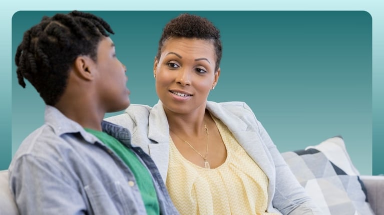 A parent and their teenage child sit on a couch, having an open and respectful conversation. The parent listens attentively, symbolizing the importance of maintaining ongoing, non-judgmental dialogue about sex, relationships, and consent during the teenage years.