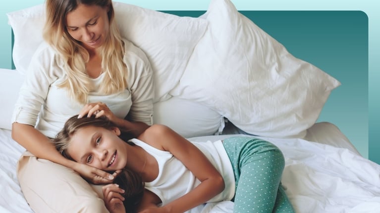 A mother and her tween daughter sit on a bed, smiling warmly at each other. Their relaxed conversation captures the need to normalize body changes, emotions, and discussions around protection and online safety as preteens navigate puberty and growing independence.