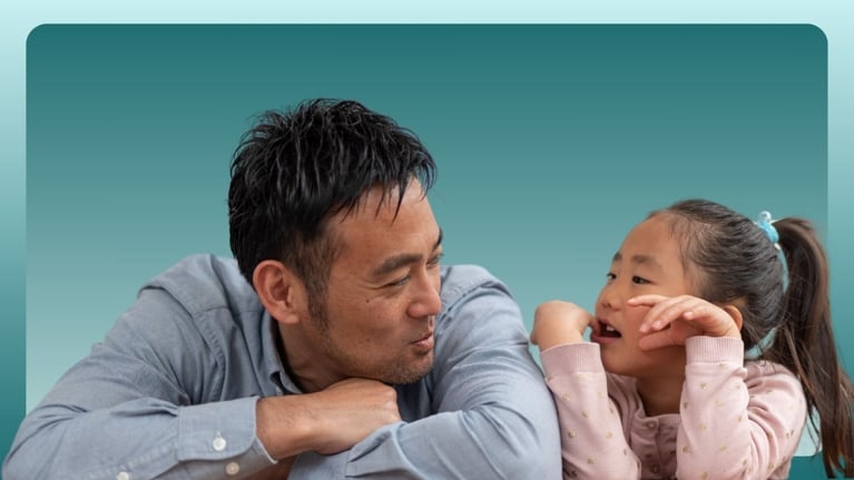 A father and his young daughter chat playfully across a table, both leaning in with animated expressions. This interaction reflects how conversations about private parts, consent, and early understanding of puberty can be woven into casual, everyday moments with kids aged six to eight.