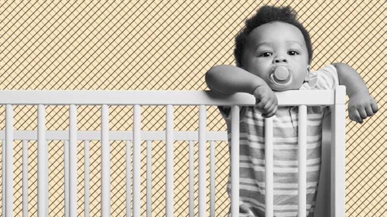 a photo of a baby with a paci standing in their crib