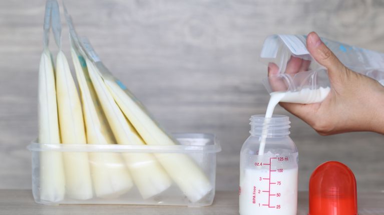 woman pouring milk in to bottles for new baby on wooden table