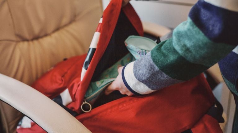 A person's arm is reaching into a red backpack or bag. Their hand is inside the bag, searching for something.