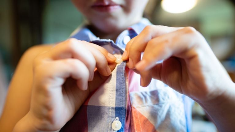 A person's hands are shown buttoning a colorful plaid shirt. They are fastening a white button through a buttonhole.