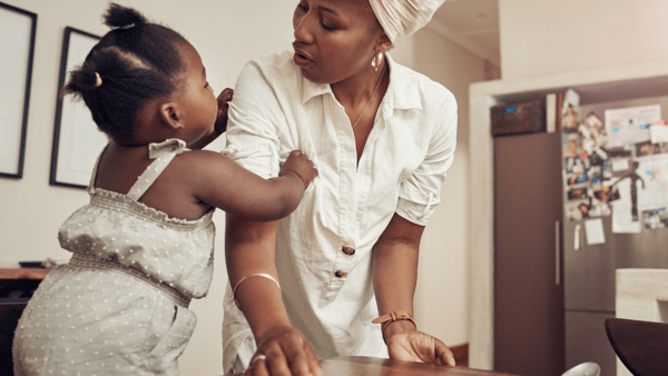 Mom wiping the kitchen table while baby daughter pulls on her for attention
