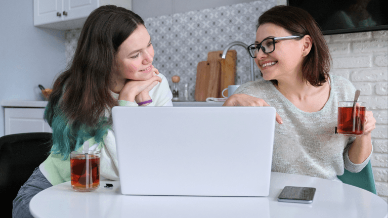 mom and daughter sitting at a table in front of a laptop talking