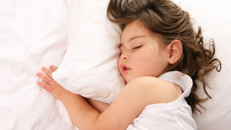 A young child with dark hair sleeps peacefully on a white pillow.