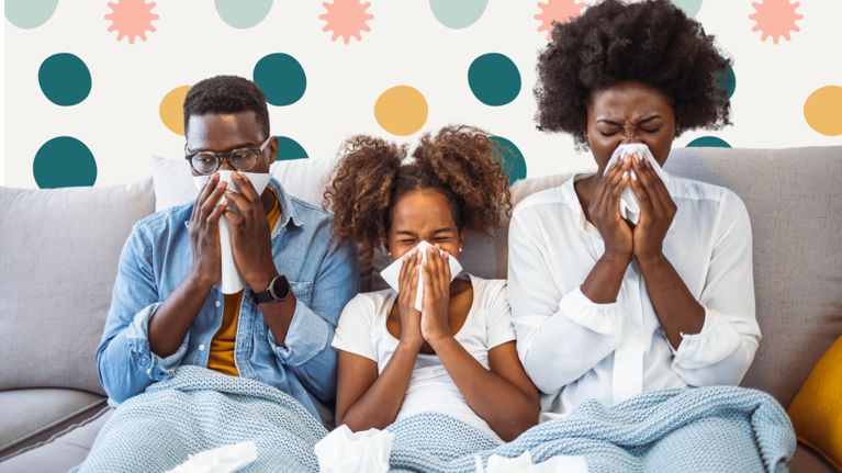 This image shows a family sitting on a couch, all appearing to be sick as they sneeze into tissues. The background features a playful pattern of colorful dots and germ-like shapes, emphasizing the theme of illness, possibly related to daycare germs spreading at home. The cozy blankets suggest they are resting while dealing with their symptoms.