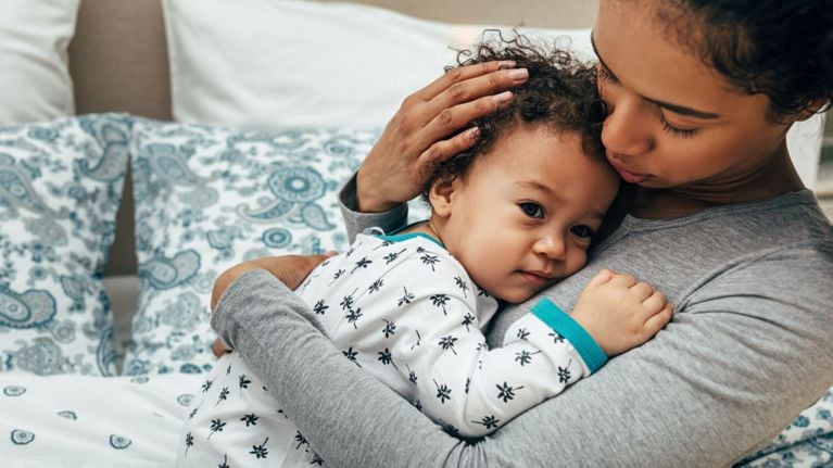A mother gently holding her toddler close in a comforting embrace on a bed.