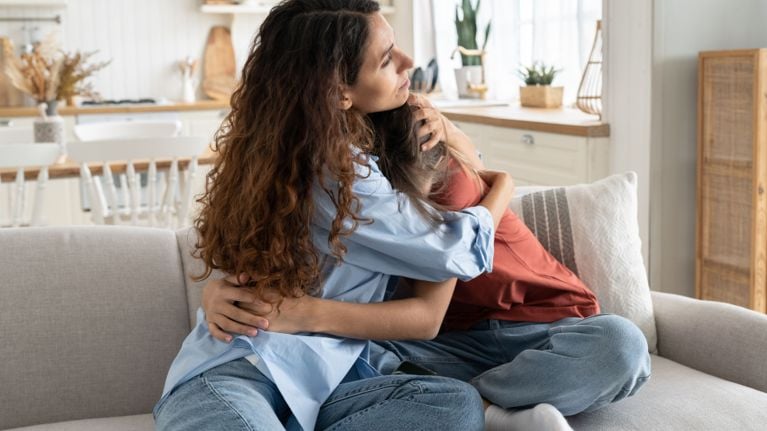 A parent and child sitting on a couch, locked in a close, reassuring hug, conveying emotional connection and co-regulation.