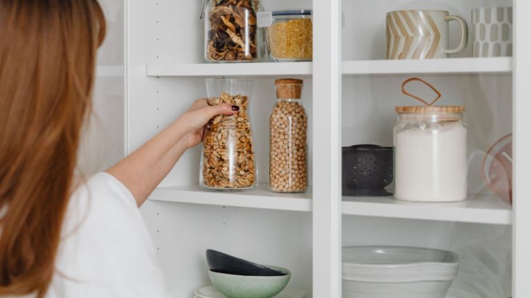 A person placing a jar of walnuts on a neatly organized shelf filled with dry goods in matching containers.