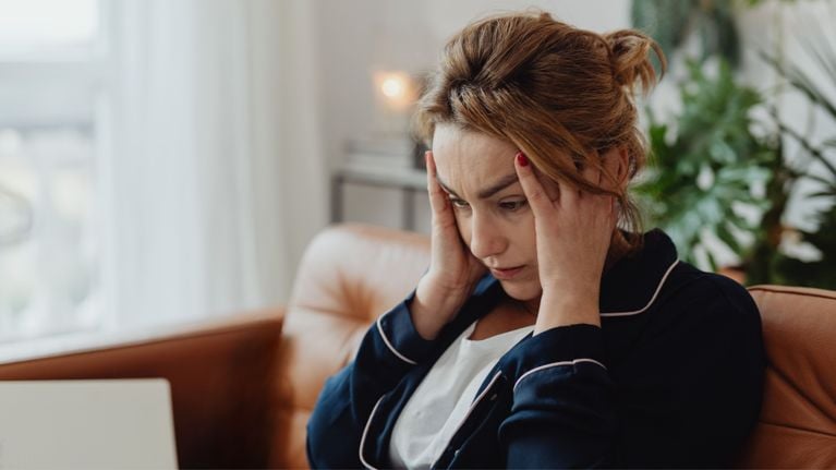 A woman sitting with her hands on her temples, looking stressed and fatigued, illustrating the emotional toll parenting a neurodivergent child can take.