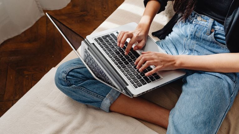 A person sits cross-legged on a couch using a laptop, suggesting online activity such as browsing social media or forums.