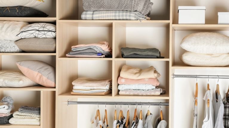 A neatly arranged open closet with folded clothes, pillows, and neutral tones organized in cubbies.