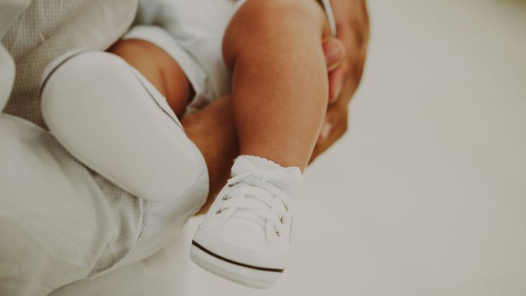 A parent cradles their baby, who is wearing sneakers. 