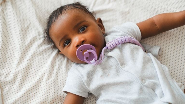A close-up on a baby wearing a pacifier as he looks into camera.