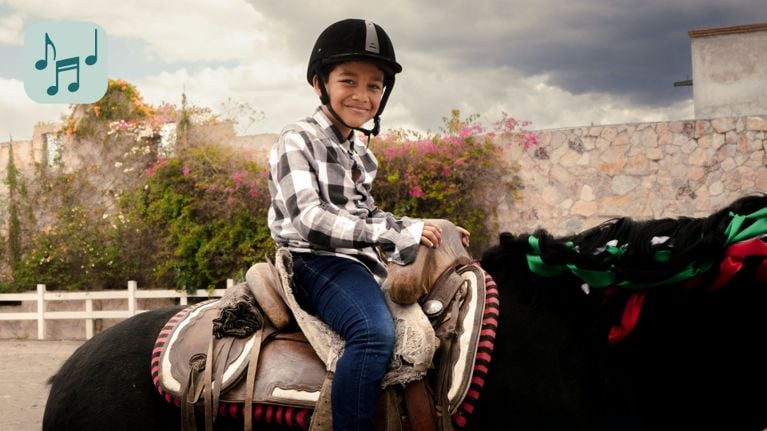 A young person is riding on the back of a brown horse outdoors. The horse is walking on green grass.