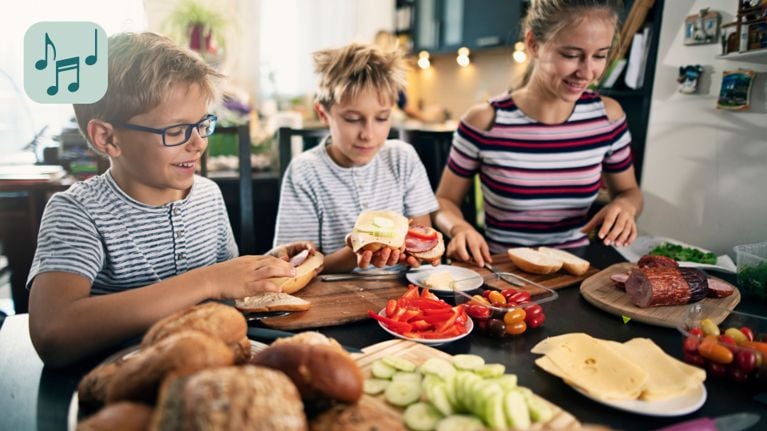 Several children are gathered around a table, some holding sandwiches. They appear to be enjoying a meal or snack together.