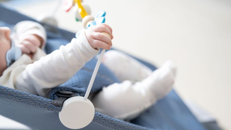 A baby wearing a onesie sleeps in his crib.