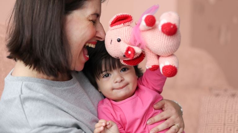 Smiling mother in her 40s playing with her baby and a pink plush toy, capturing a joyful moment of bonding and laughter.