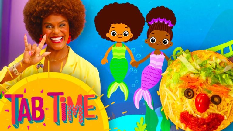 Tabitha Brown smiles brightly against a rainbow-toned background, making the ASL sign for “I love you.” Animated Black mermaid characters swim nearby, with a smiling veggie face pizza on the right. “Tab Time” is written in colorful bubble letters.