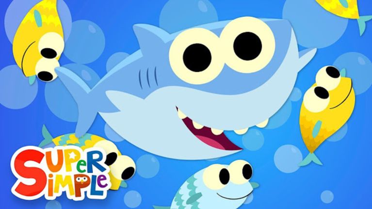 A cheerful blue cartoon shark swims with a group of big-eyed yellow and green fish on a blue bubbly background. The “Super Simple” logo is in the bottom left.