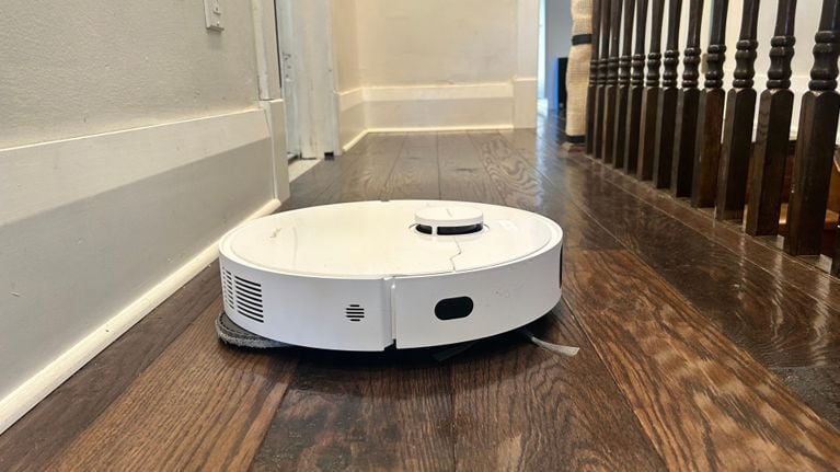 Dreame L40s Ultra CE robot vacuum actively cleaning a hallway with dark wood floors, navigating near baseboards and under stair railings.