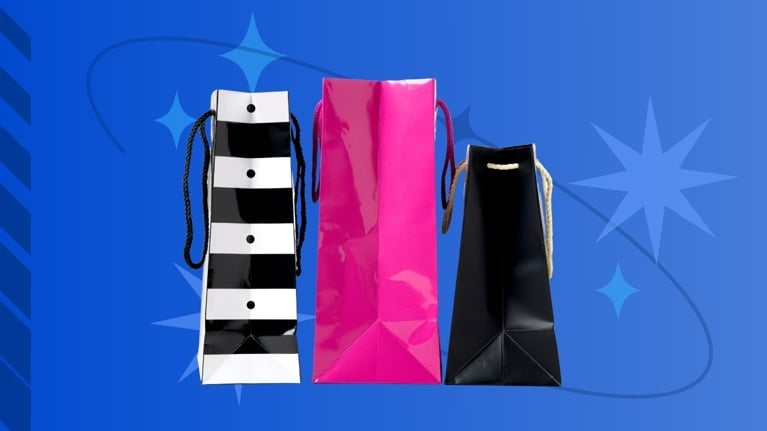 Three glossy shopping bags—black and white striped, hot pink, and solid black—stand upright against a blue backdrop with star graphics, symbolizing a beauty product haul.
