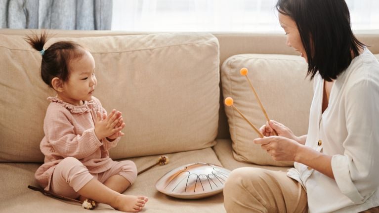 A woman sitting on the couch with a toddler and playing a percussion instrument