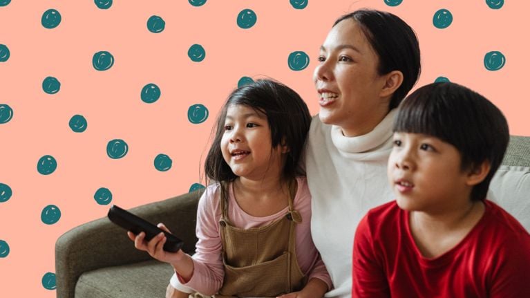 A mother and two kids sit together. One child holds a remote control.