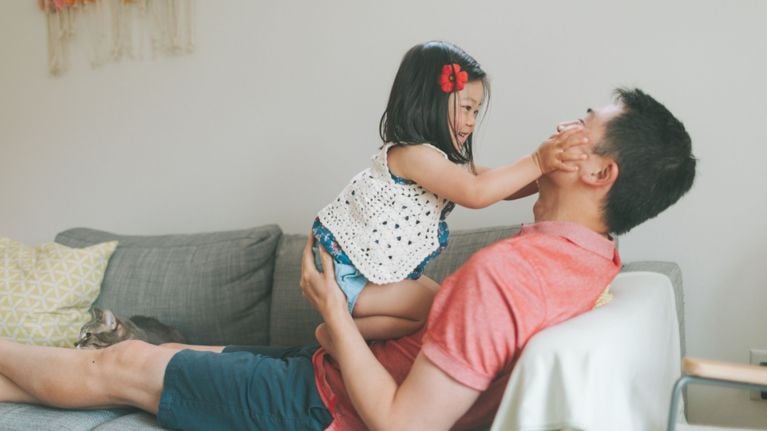 A toddler grabs her dad's face as he carries her.