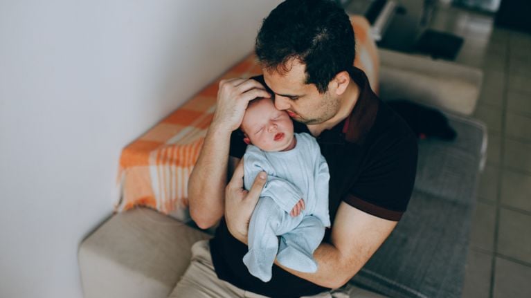 A father cradles an infant, who is facing camera.