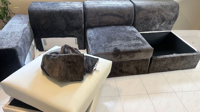 Partially assembled Cozey Atmosphere modular couch with exposed storage compartments and cushion covers laid out on the floor.