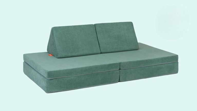 A simple, fully assembled Nugget couch in sage green upholstery is displayed against a pale blue background, showcasing its modular shape and clean lines.