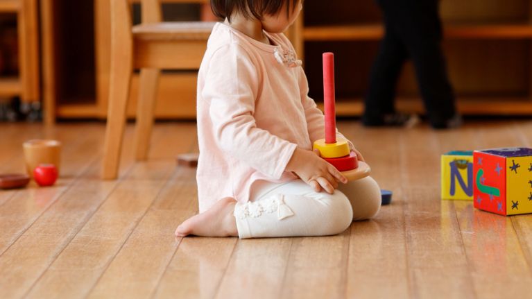 A toddler holds a wooden stacking toy.