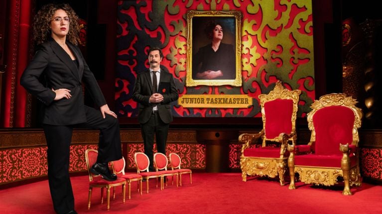 The Taskmaster and Assistant stand on the set of Junior Taskmaster. 