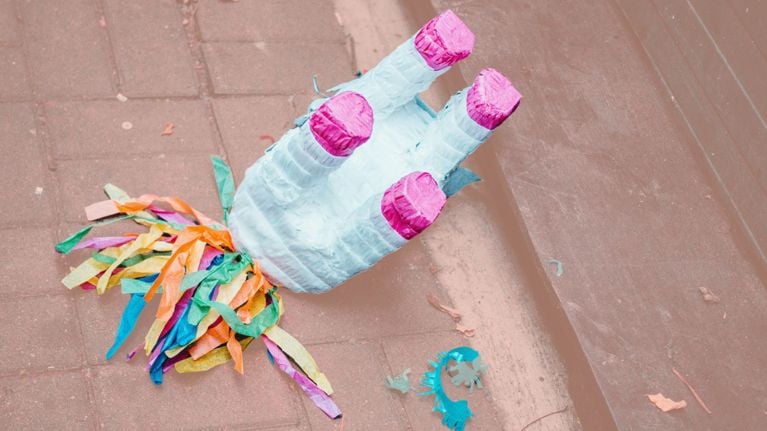 A broken unicorn piñata with pink hooves and colorful streamers lying on the pavement, evoking the aftermath of a children’s birthday celebration.