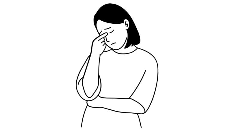 A woman stands with her arms crossed, eyes closed, and pinching the bridge of her nose, showing signs of stress and exhaustion.
